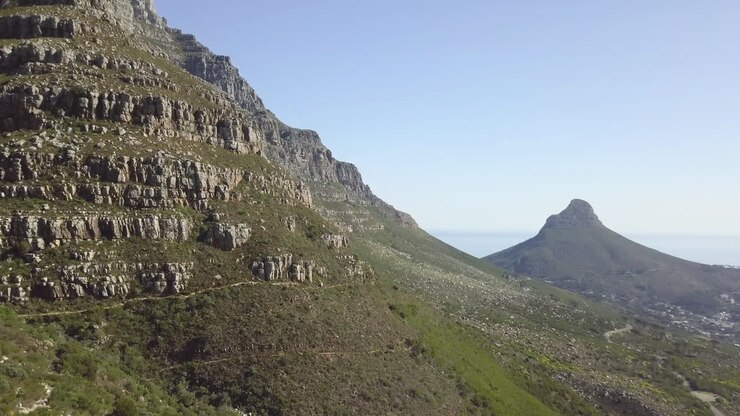 Filmato aereo 4K di alta qualità con cielo blu e soleggiato della spettacolare e panoramica montagna Lion's Head, colline rocciose con sentieri escursionistici, panorama costiero dell'Oceano Atlantico nel Capo Occidentale, Città del Capo, Sudafrica