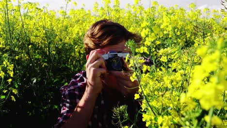 Man-taking-picture-from-camera-in-mustard-field