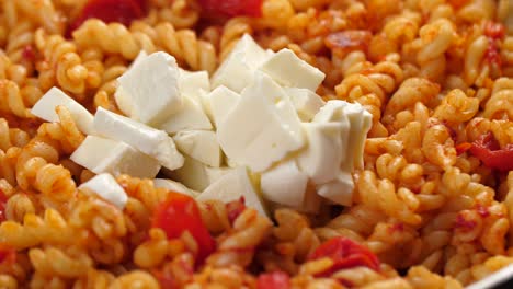 Dejando-Caer-Trozos-De-Mozarella-En-Una-Sartén-Con-Pasta-Fusilli-Cocida-Con-Salsa-De-Tomate,-Primer-Plano-En-Cámara-Lenta