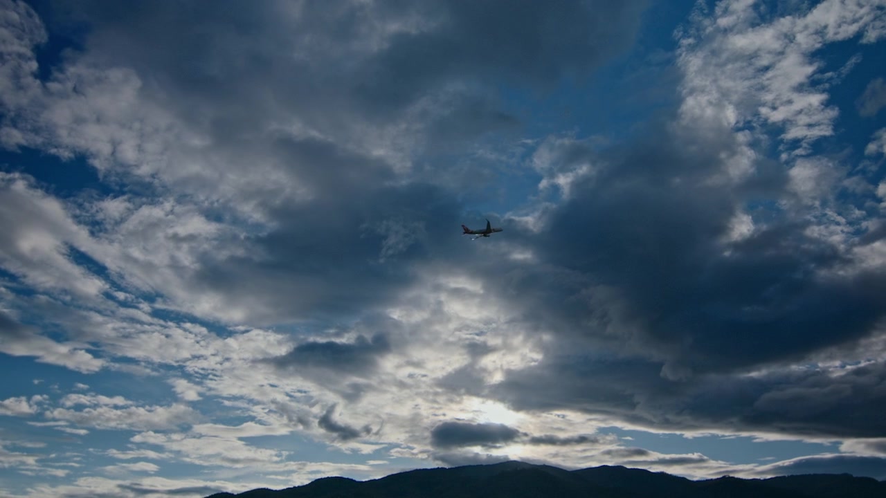 Passagerfly flyver hen over en skyet himmel over bjerge
