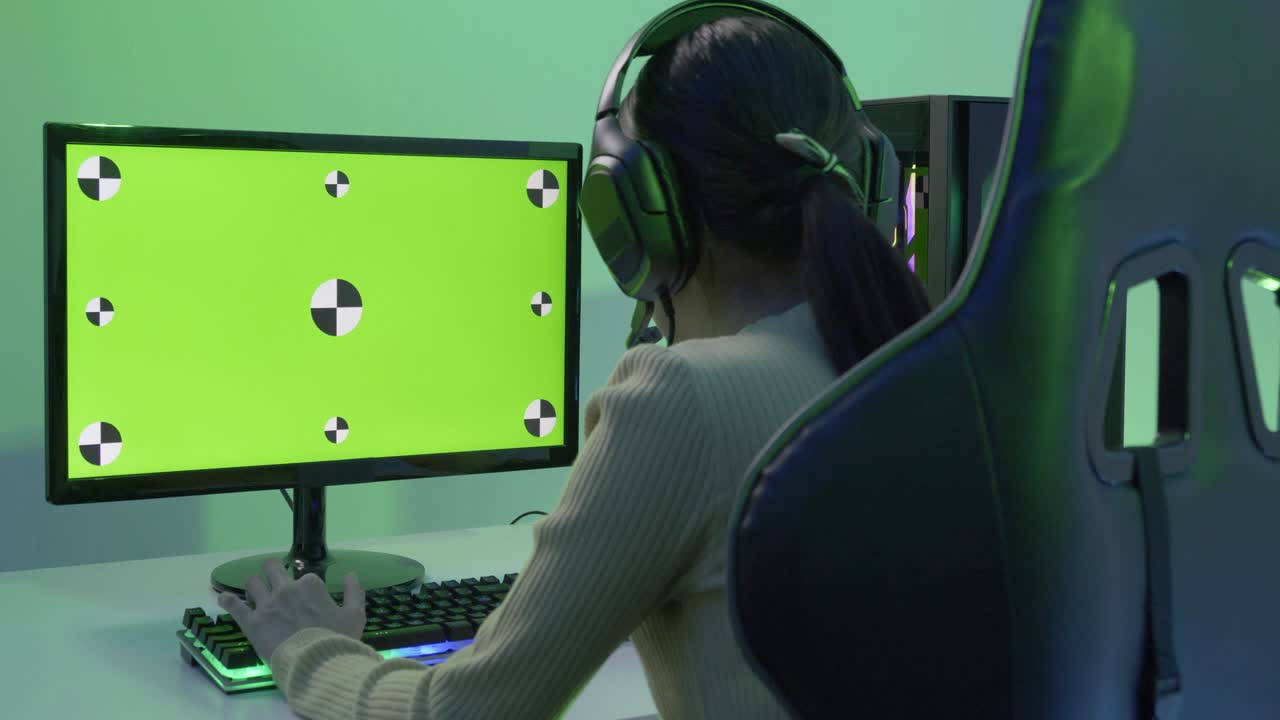 Female gamer playing game at home. Focus on green screen background inside monitor.