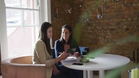 retrato de dos mujeres de negocios caucásicas sentadas a la mesa, usando una tableta y hablando