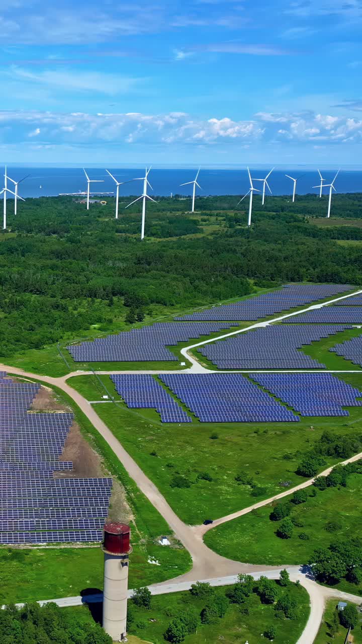 Solar panels and wind turbines with clear skies and green landscape, aerial view