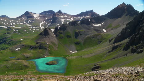 vista aérea cinematográfica superior cuenca del lago de hielo isla de silverton lago aqua azul agua clara tundra alpina impresionante cordillera nieve flores silvestres mediados del verano durante el día hermosa panorámica lenta a la derecha