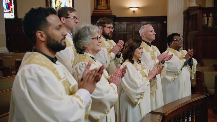 Clapping robed church choir members at choir rail in nave, front-left initiating applause in thanks