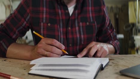 man writing in notebook in workshop