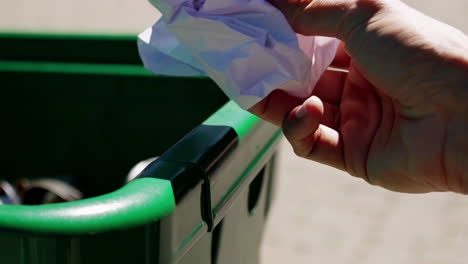 person throwing crumpled paper into a green recycling bin