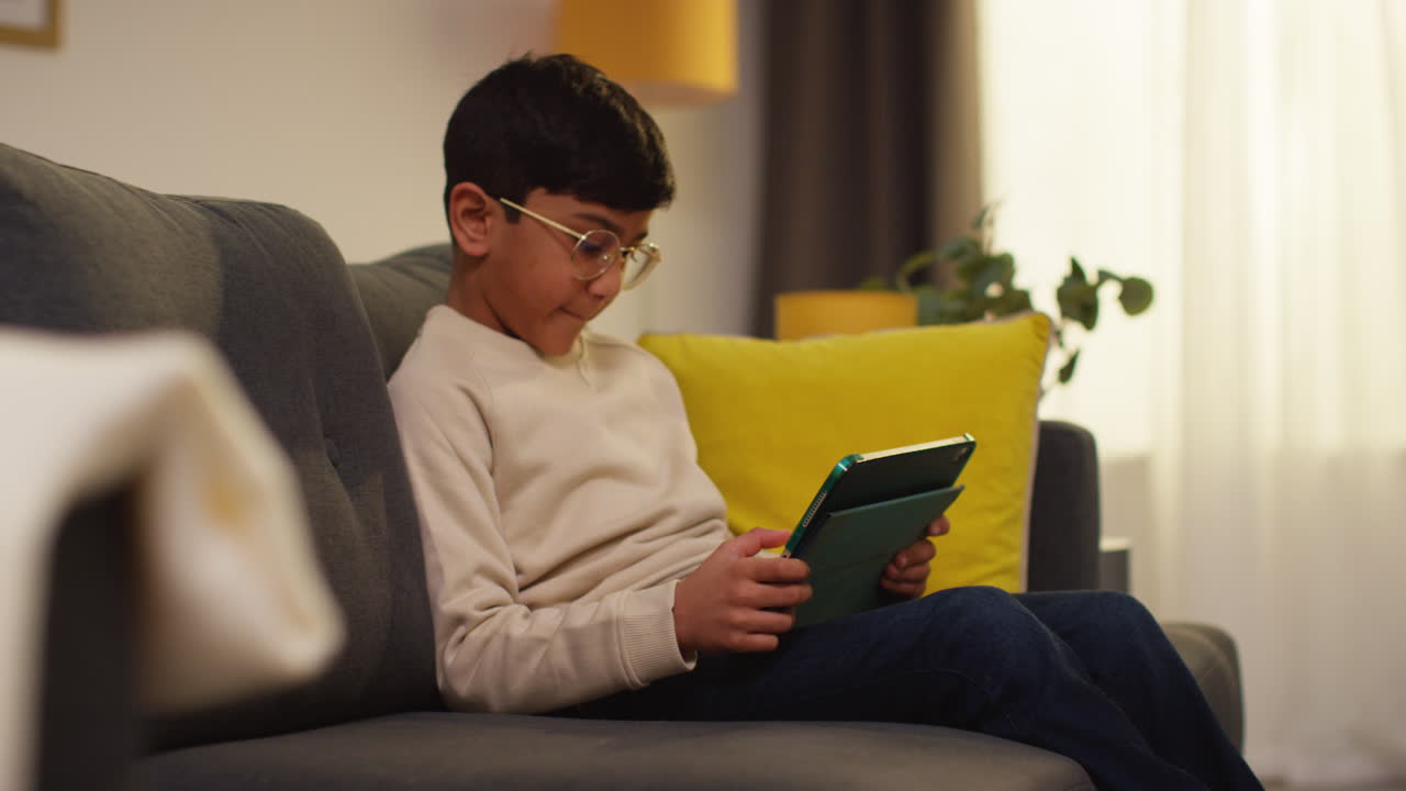 Young Boy Goes To Sit On Sofa At Home And Play Games Or Stream Content Onto Digital Tablet 1