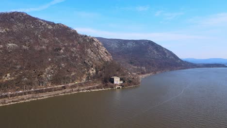 aerial drone footage approaching breakneck ridge in the appalachian mountains over a river in new york's hudson valley during early spring at the hudson river with blue skies