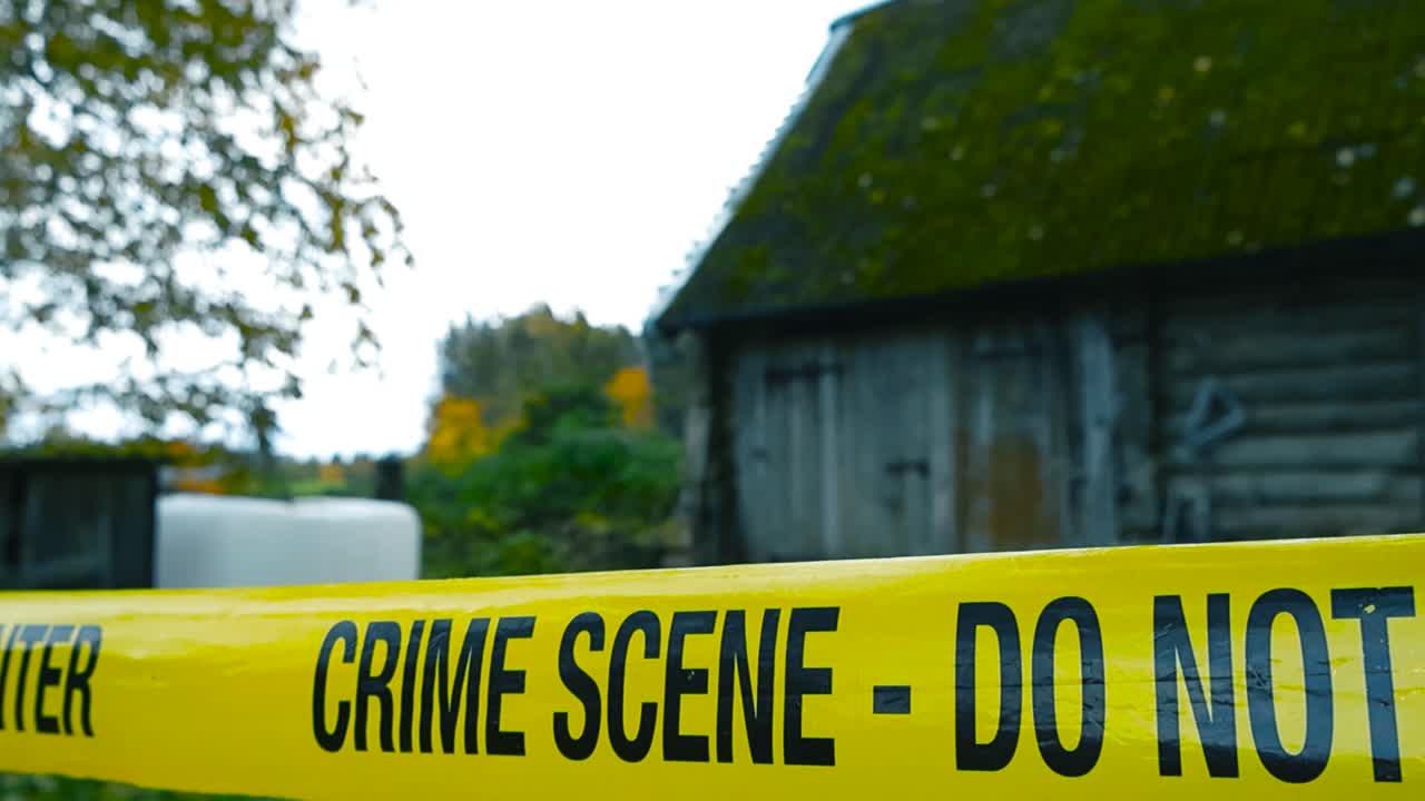 Close up view of a yellow police line or crime scene forensic investigation tape in front of an old vintage countryside farmhouse with autumn trees around with yellow leaves, Bokeh blurry background