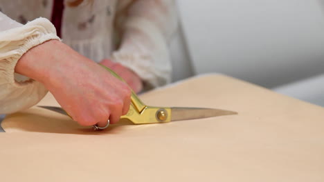 young female designer with tape-line on her neck standing in dressmaking studio and drawing lines with chalk and rule. female couturier in atelier cutting out a pattern for future clothes.