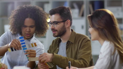 gruppo multietnico di giovani designer che utilizzano campioni e discutono insieme le opzioni di colore per il progetto