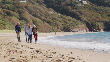 senior couple walking along shoreline with adult offspring on winter beach vacation