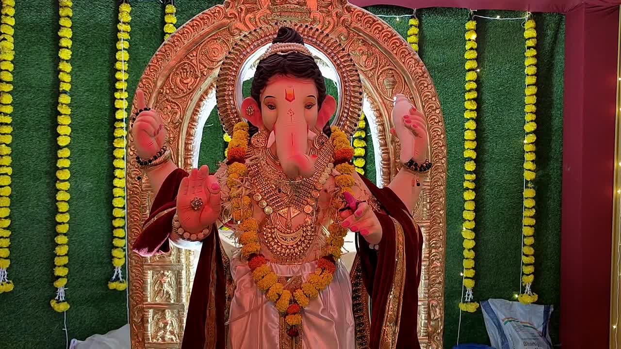 Camera slowly ascends to stunning statue of Lord Ganesha, illuminated by vibrant multicolored lights, with backdrop of artificial grass in pandal during Ganesh festival in India.