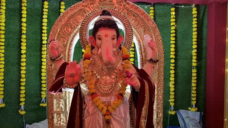 camera slowly ascends to stunning statue of lord ganesha, illuminated by vibrant multicolored lights, with backdrop of artificial grass in pandal during ganesh festival in india.