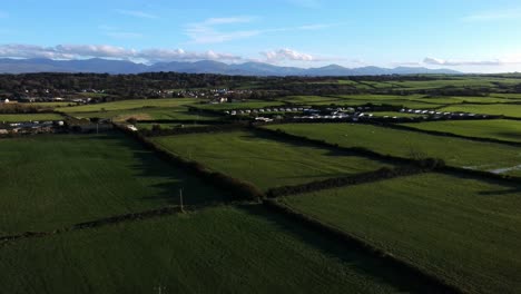 Vista-Aérea-De-Las-Sombras-Del-Atardecer-Sobre-Los-Prados-De-Tierras-De-Cultivo-De-Anglesey-Bajo-La-Cordillera-De-Snowdonia