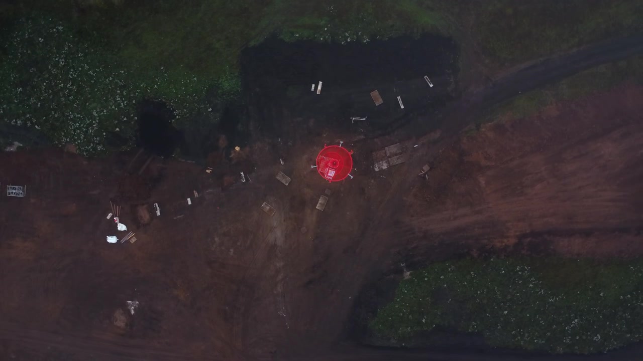 Aerial top-down view of a dirt road crossing dense green vegetation, with a small red object near the center and scattered light-colored items around it in