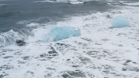 stunning drone shot of waves breaking on beautiful ice rocks at diamond beach in iceland