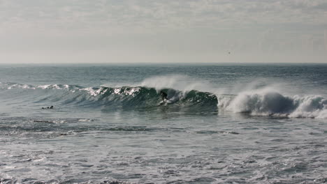 Un-Surfista-Desaparece-Mientras-Otro-Coge-Una-Buena-Ola-Surfeando-Hacia-Una-Puesta-De-Sol-Dorada