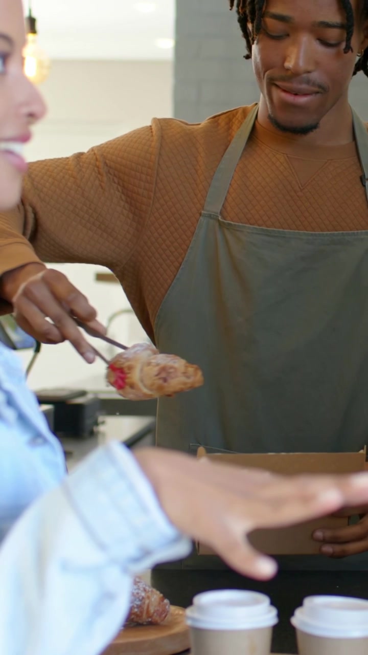 Video verticale: Cliente che ordina, barista con grembiule che confeziona un dolce in una scatola con le pinze al bancone del caffè.