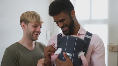 same sex male couple with baby daughter in sling by front door of house