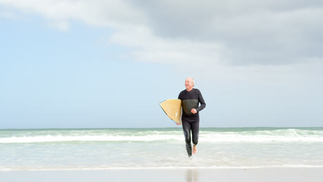 Vorderansicht-Eines-Alten-Kaukasischen-älteren-Mannes,-Der-Mit-Surfbrett-Am-Strand-Läuft-4k