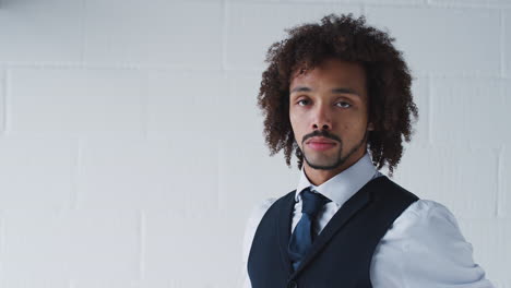 portrait of young businessman in suit fastening tie standing against white studio wall