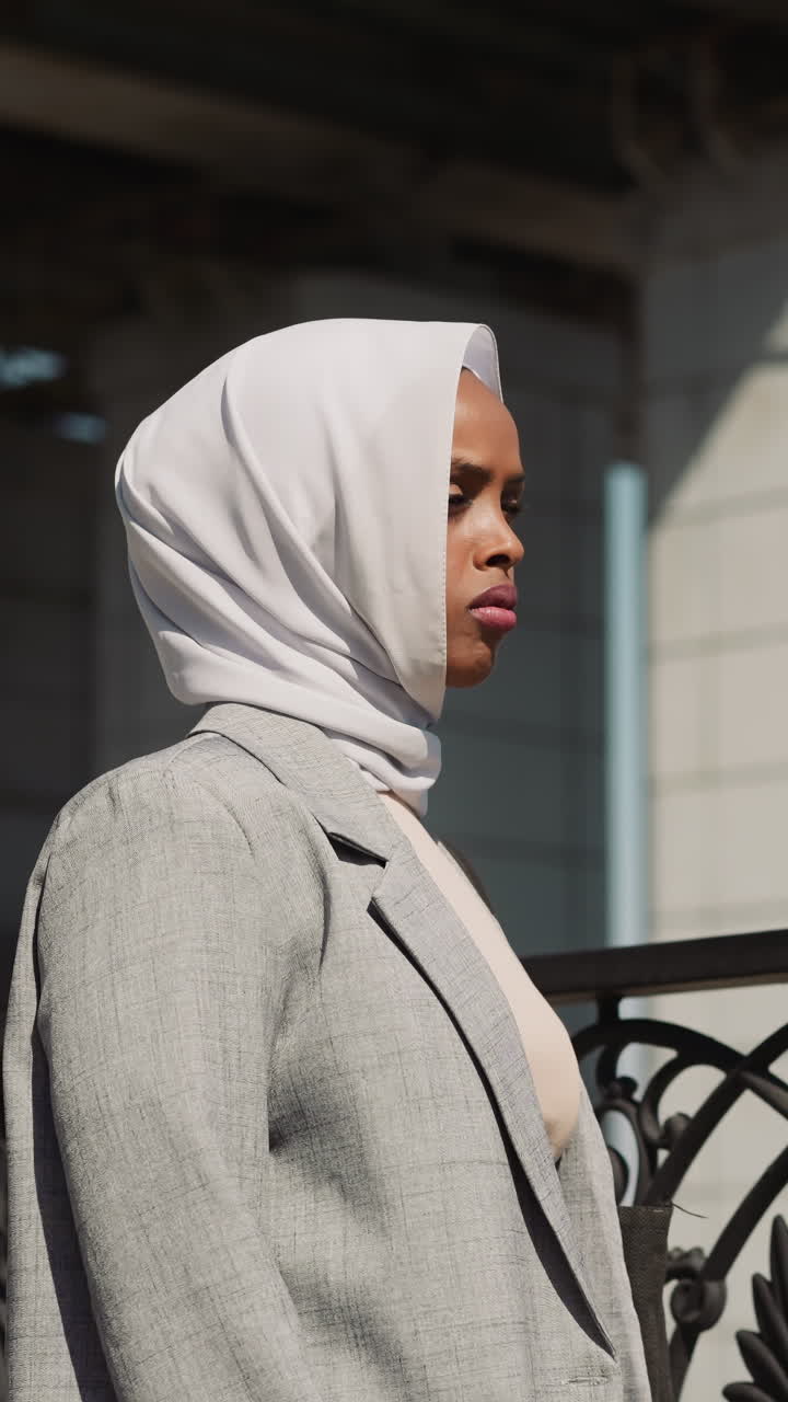 Sad Arabian woman with white hijab stands by fence on embankment close view. African-American lady against city overpass bridge. Urban architecture