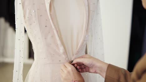 unrecognizable female tailor fasten foundation garment on sparkling wedding dress on mannequin in bright studio. close up of woman's hands zipping up the dress on the back