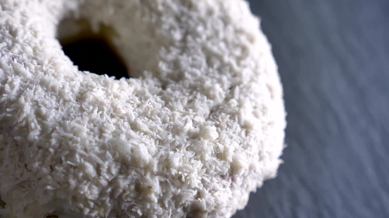 un primer plano de una rosquilla blanca con papas fritas de coco girando lentamente sobre el fondo gris de la mesa.
