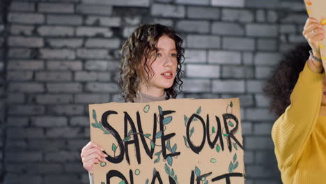 young environmental activist holding a cardboard with save our planet" inscription and protesting with her friend against climate change inaction"