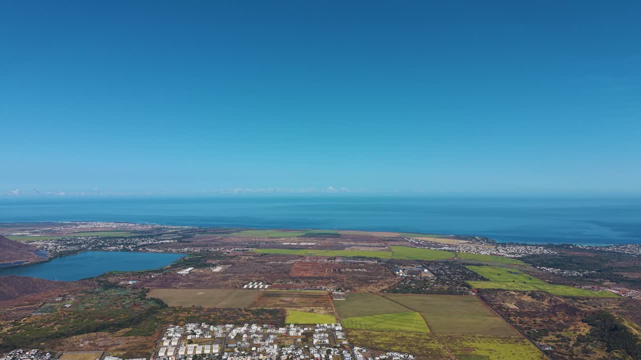 Expansive aerial view of Mauritius revealing lush fields, coastal towns, and the deep blue Indian Ocean beneath a clear sky. A serene and vibrant panorama showcasing the island’s natural beauty