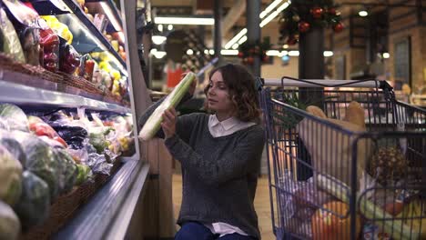 young woman in modern supermarket choosing celery leek in organic vegetable department. healthy female buying green food. concept fresh, assortment, vegetarian girl in grocery store