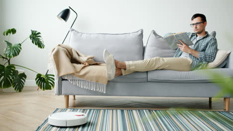 man relaxing on sofa with robotic vacuum