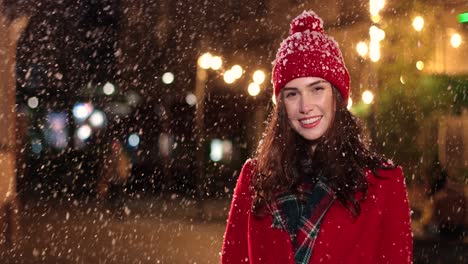 una joven alegre con abrigo rojo sonriendo a la cámara mientras nieva en navidad