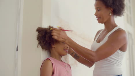 smiling black woman measuring her daughter's height at the wall and then looking at the mark