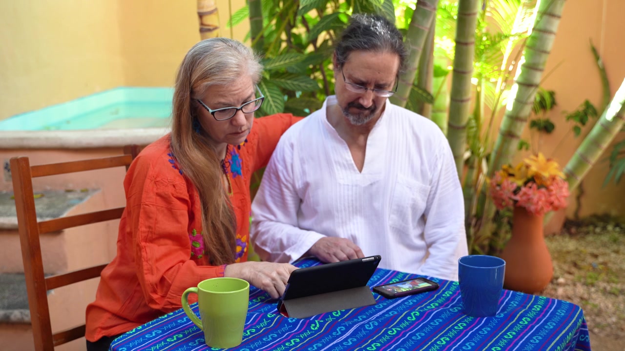 Casal maduro olha para um tablet e se inclina para vê-lo e conversar