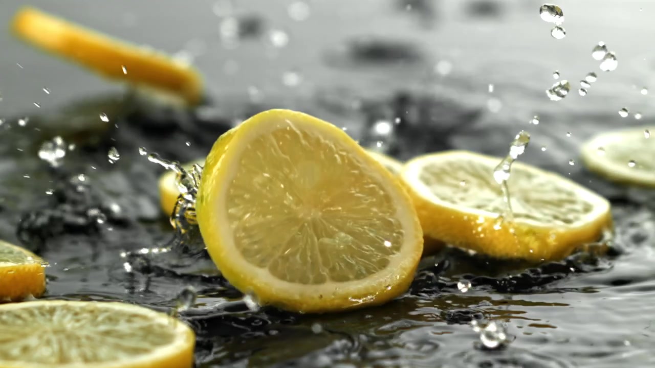 Fette di limone fresche che schizzano nell'acqua al rallentatore.