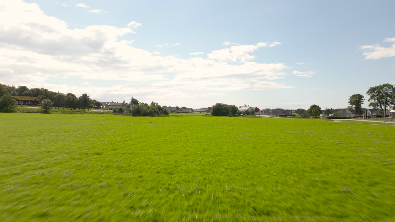 Un drone volant à basse altitude au-dessus d'un champ d'herbe et d'un terrain de sport par une journée ensoleillée