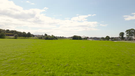 A-drone-flying-low-over-a-grass-field-and-sports-pitch-on-a-sunny-day