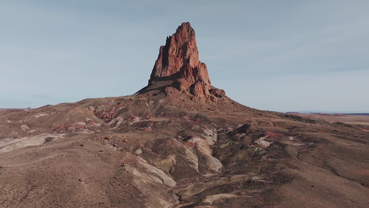 Aerial drone footage of Agathla Peak, also known locally as El Capitan, in northern Arizona. Smooth upward reveal showing the volcanic rock formation rising from the desert near Monument Valley