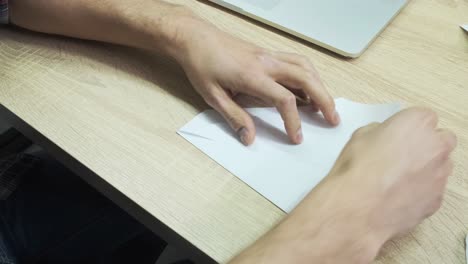 person folding a paper airplane at a desk