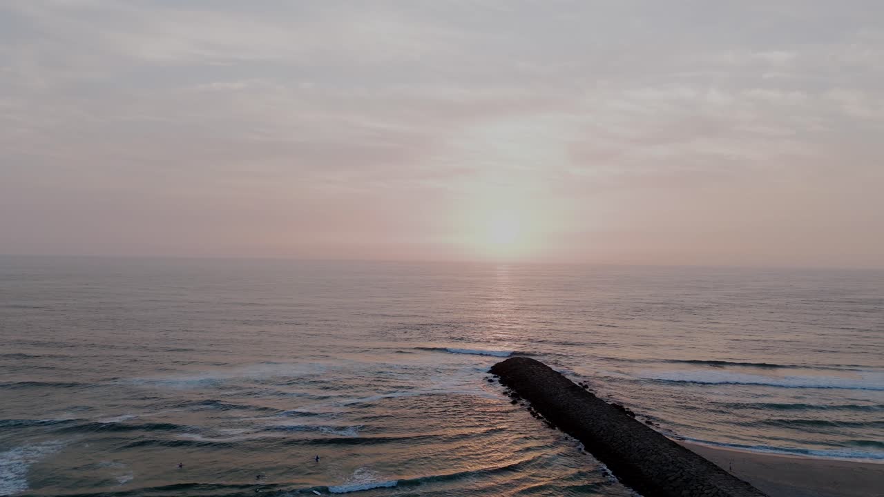 포르투갈 상페드루 오바르 마세다 해변의 돌 부두에서 서퍼들이 석양 아래 파도를 타는 항공 뷰