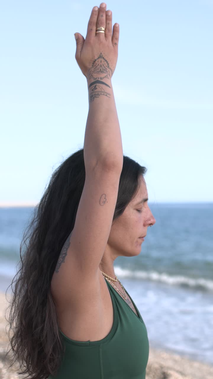 Fit female yogi meditating with hands raised at beach