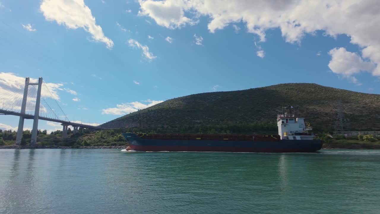 Pan left capturing a cargo ship passing under the suspension bridge of Chalkida, blending motion, architecture, and maritime scenery