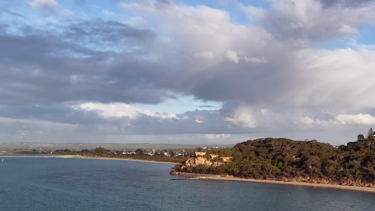Camera slowly pans across coastal headland, blue water, dramatic clouds, and natural landscape lighting
