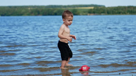 cute toddler enjoying water in the river. kid takes some water and touching his belly.