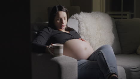 Heavily-pregnant-brunette-woman-on-sofa-and-feels-baby-bump