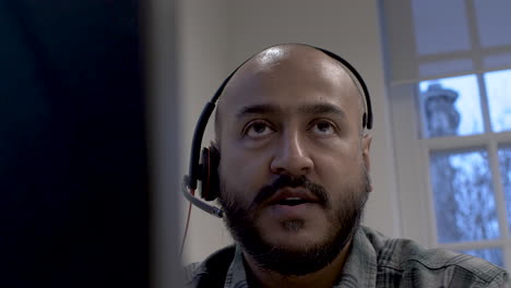 minoría étnica calva hablando con un cliente usando un micrófono con auriculares visto detrás del monitor