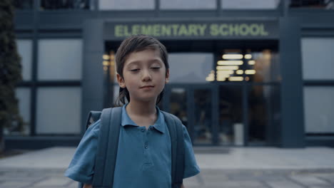 Niño-De-Edad-Primaria-Parado-En-El-Primer-Plano-De-La-Entrada-De-La-Escuela.-Colegial-Mirando-Cámara.